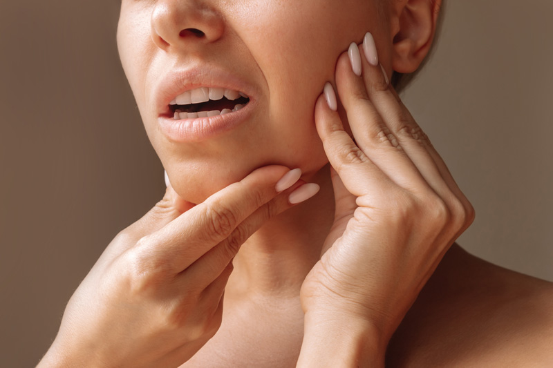 Cropped shot of young woman suffering from jaw pain holding her